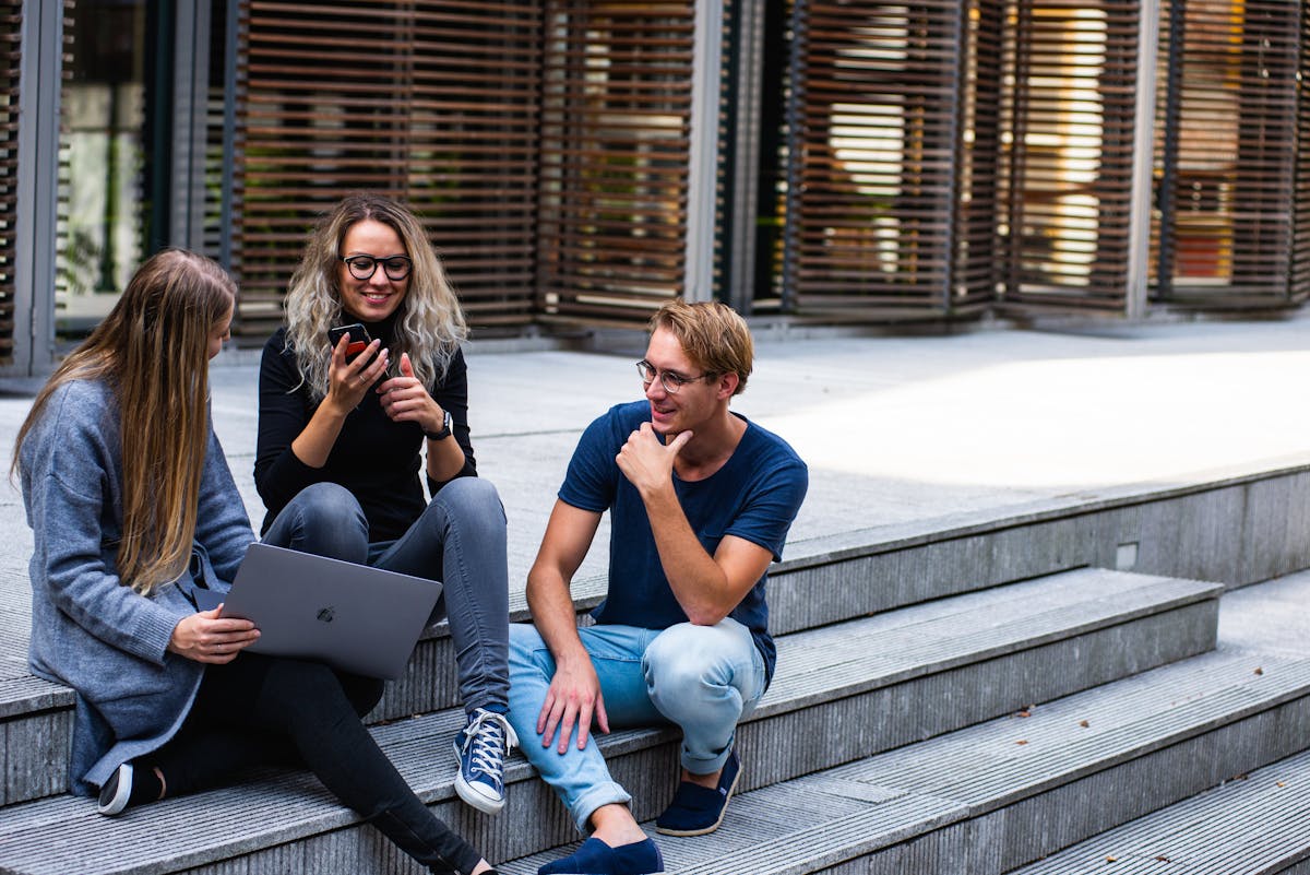 Apps que revolucionam seu método de estudo Three young professionals having a friendly chat while sitting on outdoor steps.