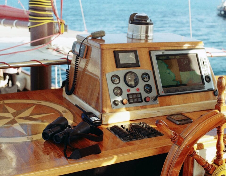 Gadgets indispensáveis para melhorar sua pescaria Wooden sailing boat helm featuring vintage control panel, navigation tools, and binoculars on a sunny day at sea.
