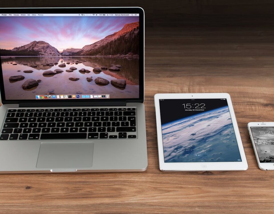 O que priorizar ao escolher dispositivos? Modern workspace showcasing Apple laptop, tablet, and smartphone on a wooden desk.