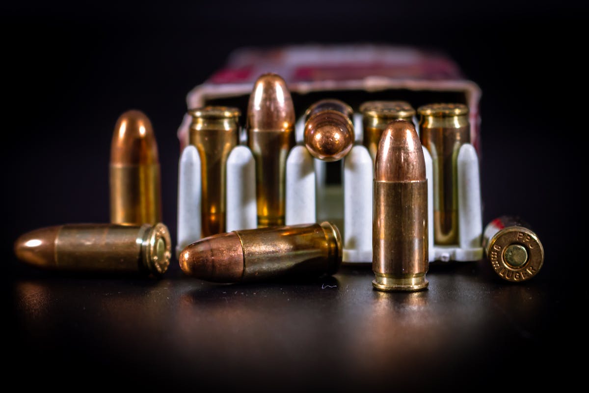 Como a tecnologia transformou a fabricação de armas Detailed close-up of copper ammunition bullets in a cardboard box on black background.