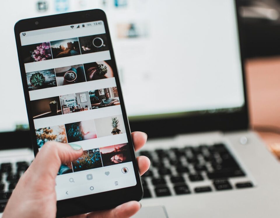 Estratégias para crescer no Instagram com IA A person uses a smartphone to browse social media in front of a laptop, emphasizing modern technology and lifestyle.