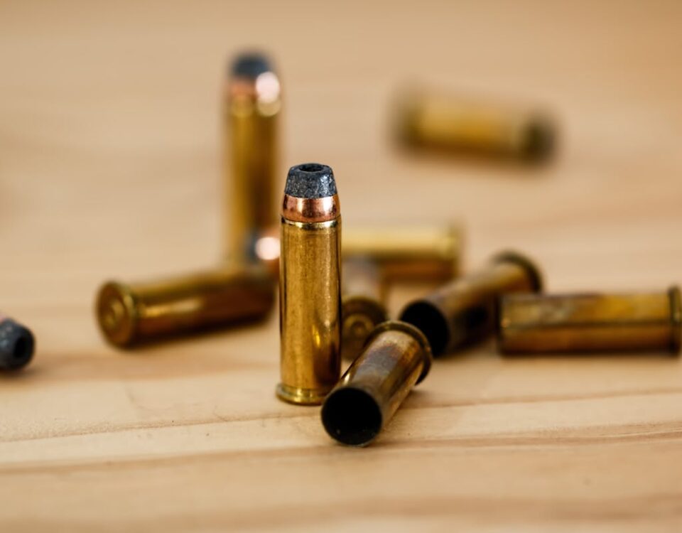 Como a tecnologia transforma o uso de armas de fogo? Detailed view of brass bullet shells scattered on a wood background.