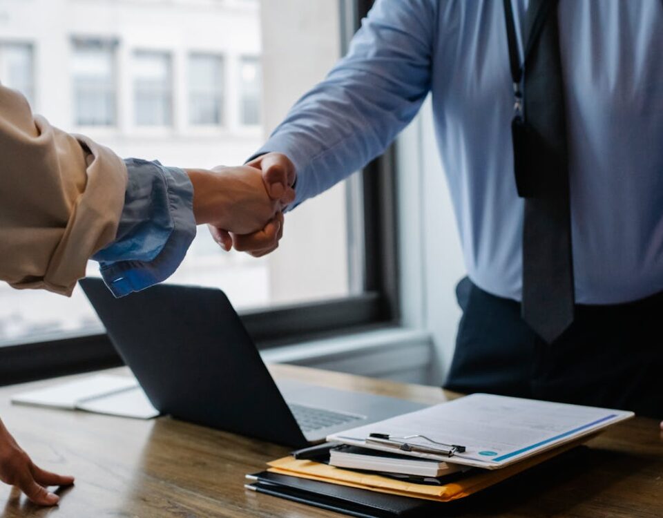 Ferramentas digitais que ajudam despachantes Crop unrecognizable coworkers in formal wear standing at table with laptop and documents while greeting each other before meeting