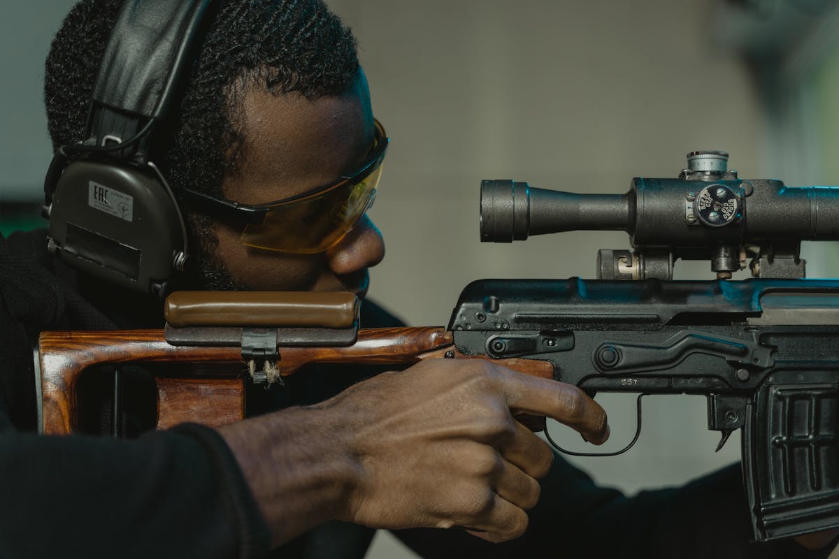 Close-up of a man aiming a rifle with eye and ear protection in a shooting range.