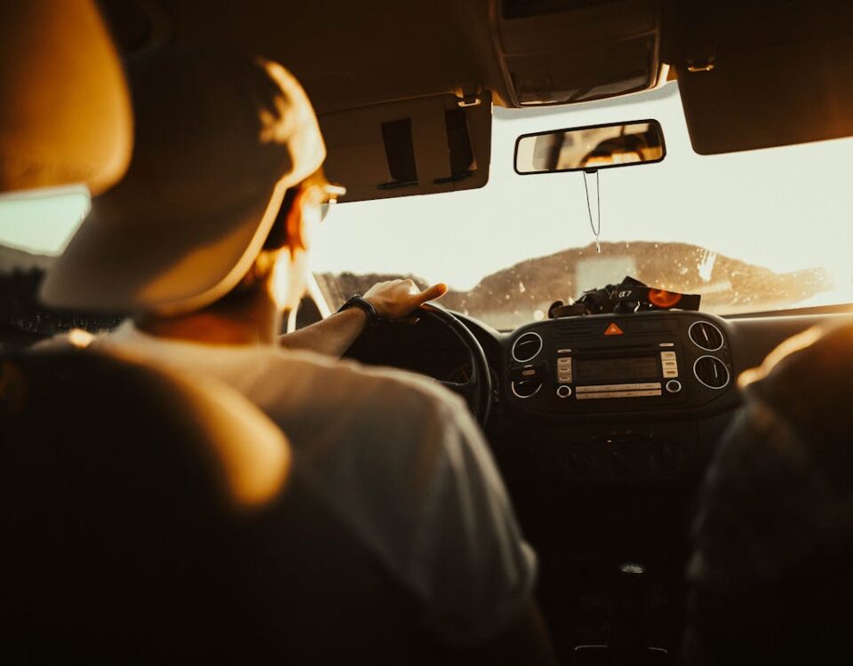 Tecnologias que revolucionam o ensino de direção Man driving car with passenger at sunset, capturing warm sunlit atmosphere.