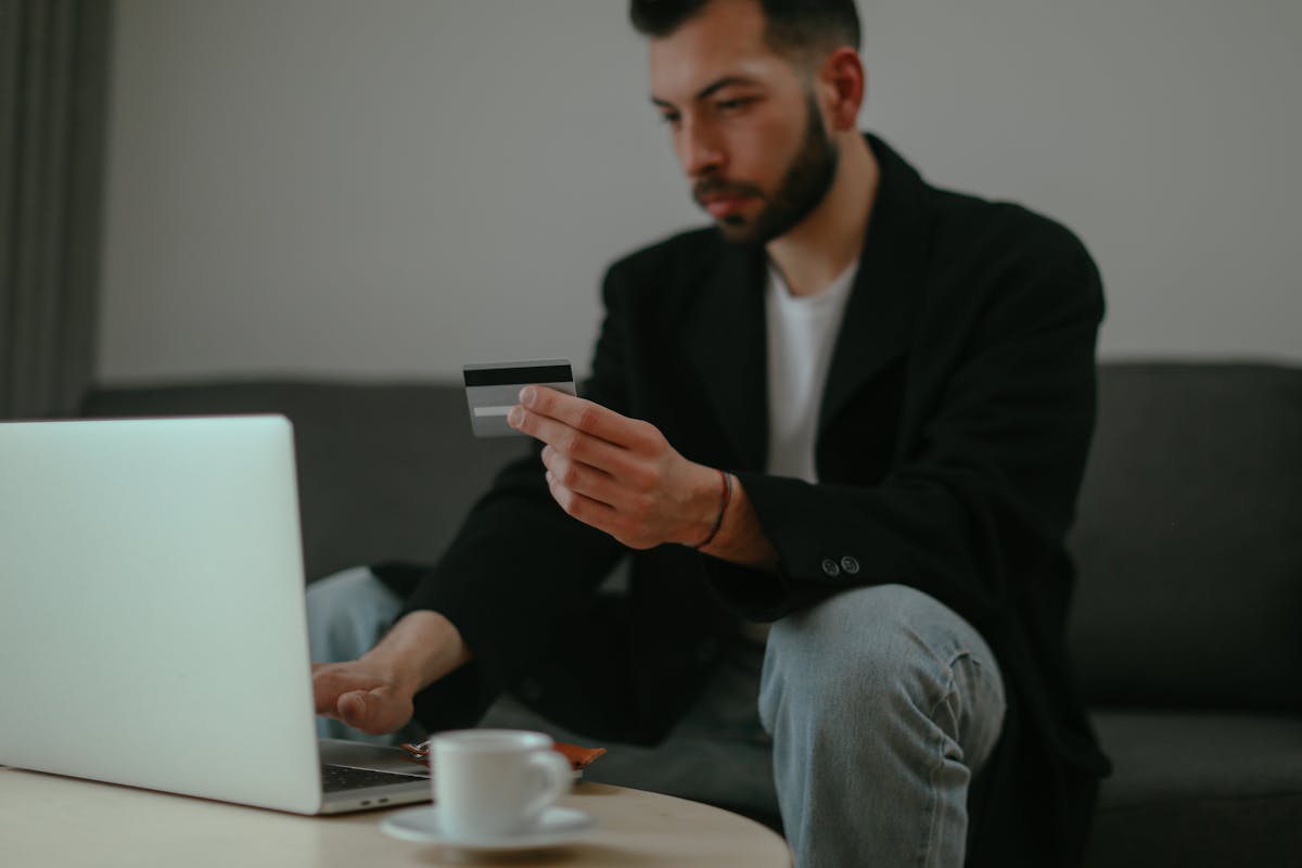 Focused man holding a credit card while shopping online with a laptop in an indoor setting.