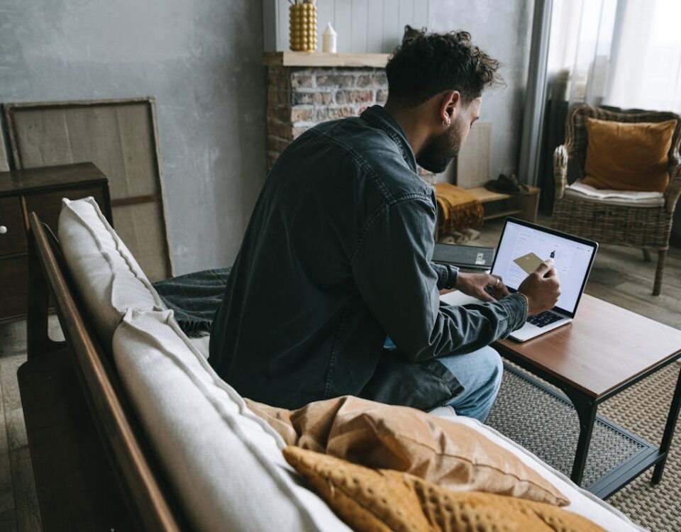 Como a tecnologia está mudando o mercado de armas A man wearing a denim jacket makes an online purchase using his laptop while sitting indoors on a couch.