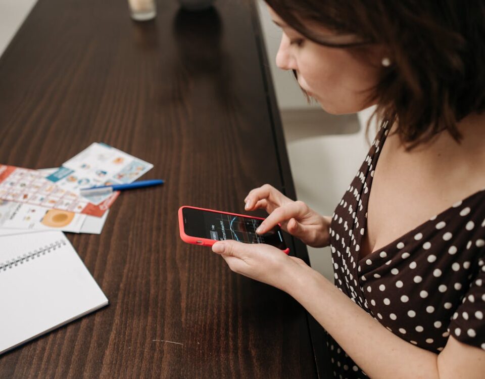 Como a IA está transformando o consumo de notícias Woman in a polka dot dress using smartphone at a table indoors with documents.
