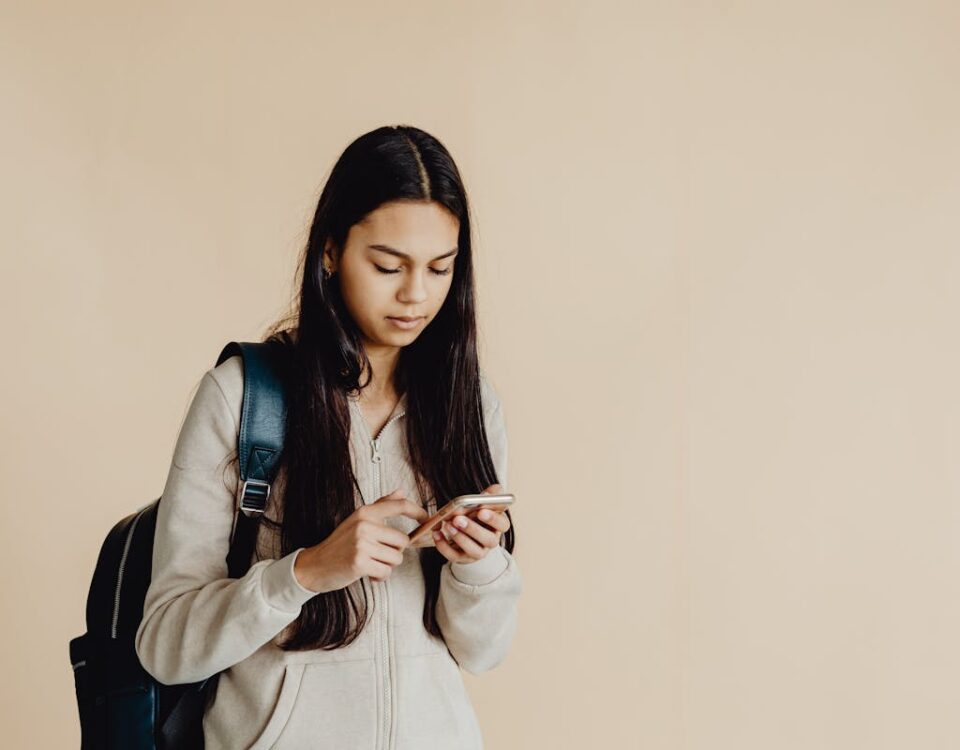 Apps indispensáveis para aprender idiomas em 2025 Teenage girl with backpack using a smartphone in a minimalist indoor setting, suited for educational themes.