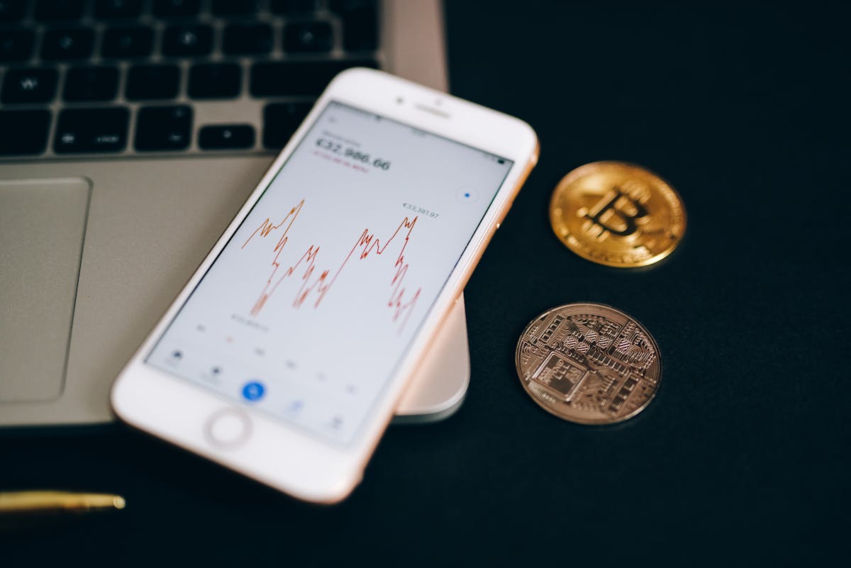 Como funciona a mineração de criptomoedas? Close-up view of cryptocurrency coins and stock market graph on a smartphone screen.