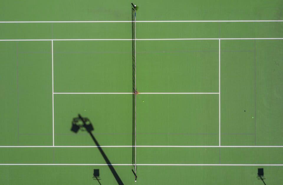 Software para gestão de arenas: guia essencial High-angle drone shot of a tennis match on a bright green court with shadows.