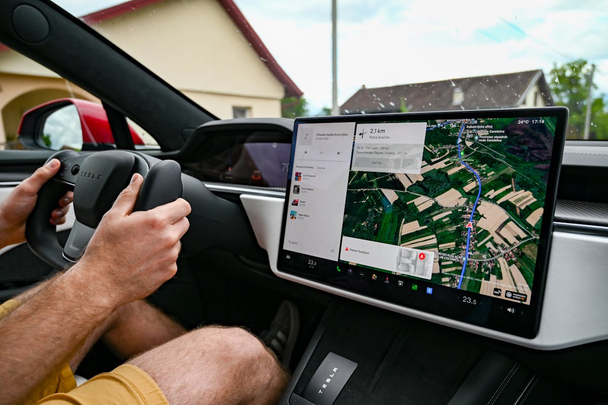 Como funcionam os carros com direção semiautônoma Man driving Tesla using GPS on touchscreen dashboard for navigation.