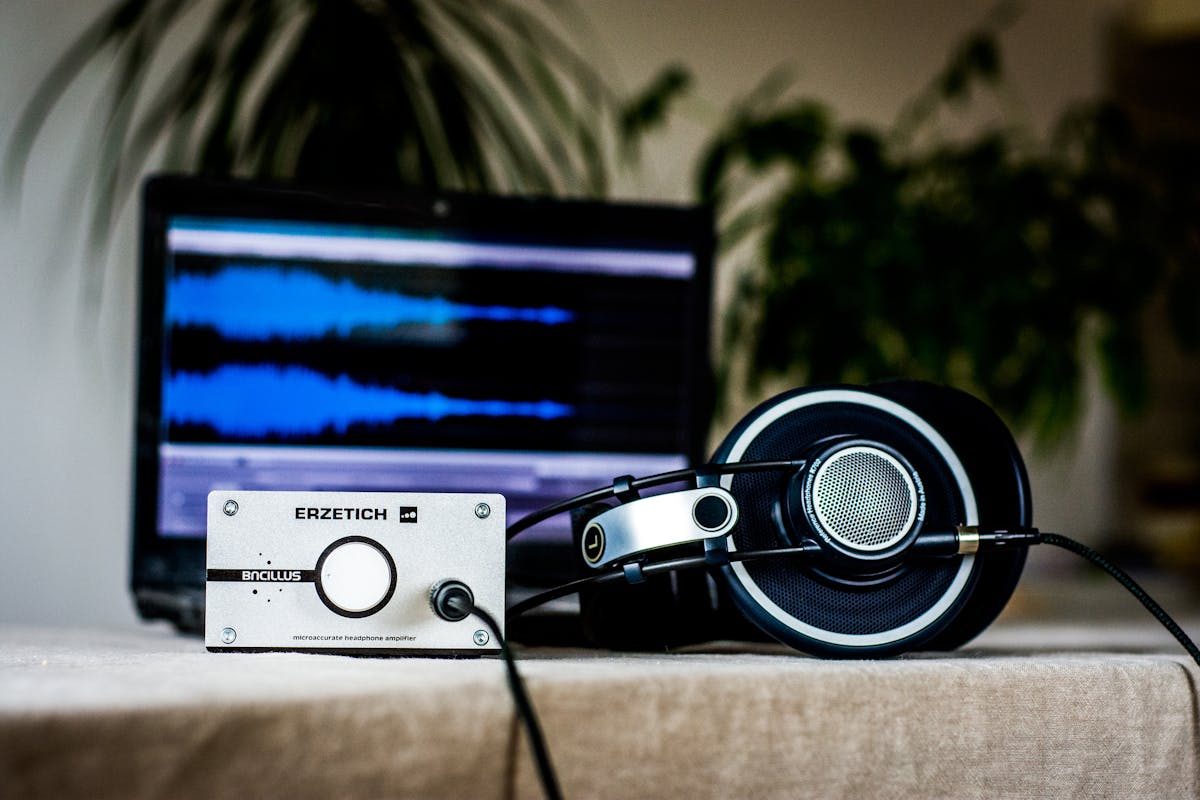 Qual a diferença entre drivers de áudio e codecs? A sleek setup featuring headphones and an amplifier in front of a sound editing laptop, ideal for audio professionals.