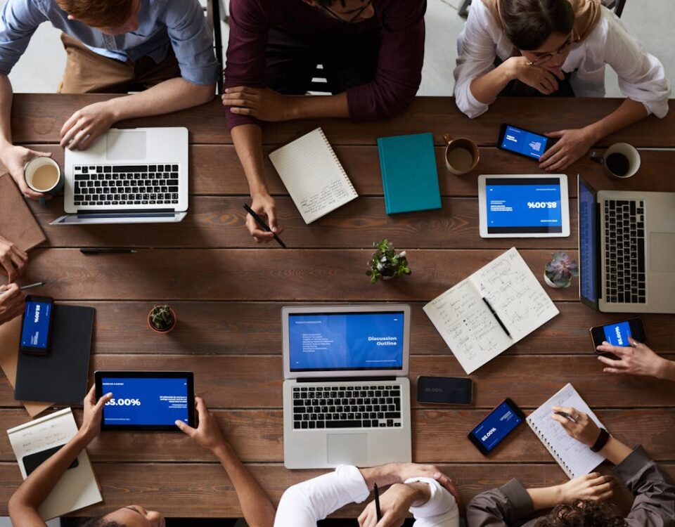 Como a tecnologia eleva os serviços de agências criativas Overhead view of a diverse team in a business meeting using laptops and tablets.