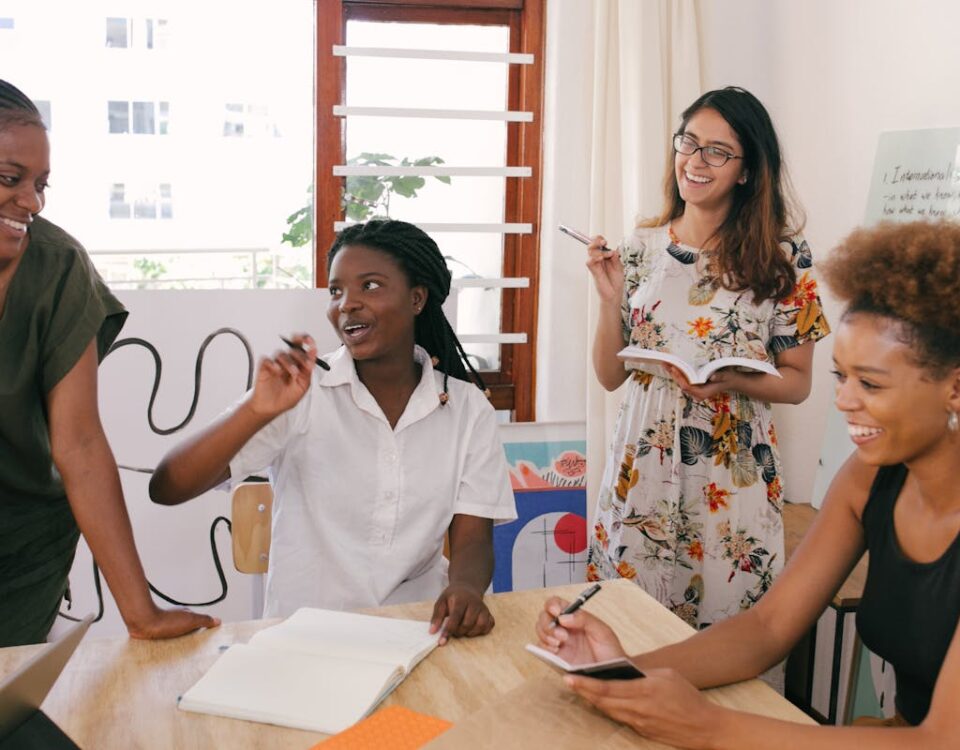 5 práticas de TI para acelerar processos empresariais A diverse group of women engaged in a lively office meeting, sharing ideas and brainstorming together.