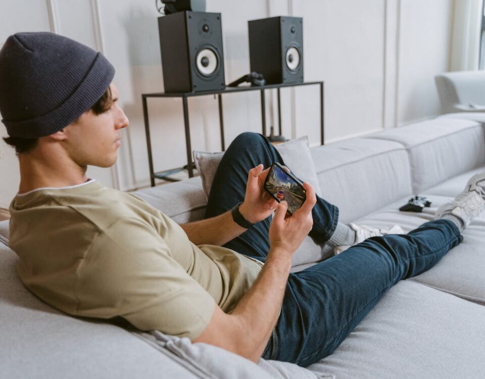 Apps para treinar direção e estudar para a CNH Casual young man playing mobile games on sofa with speakers in the background.