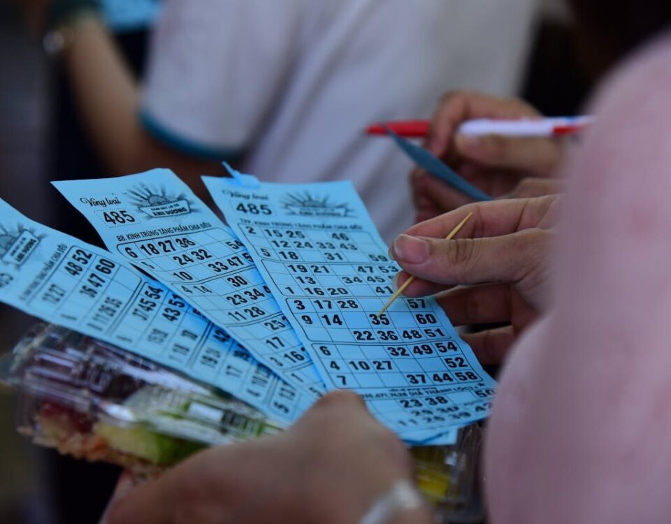 People playing bingo indoors, holding blue bingo cards with pen and markers.