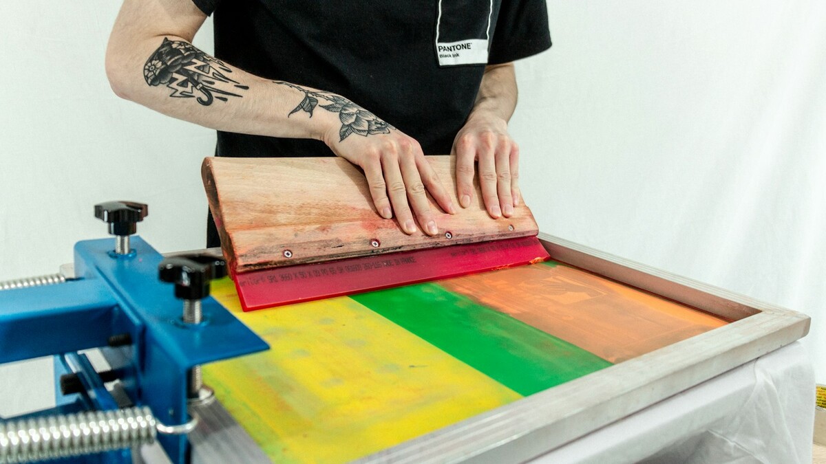 Estampador passando rodo sobre tela de serigrafia com tintas coloridas
