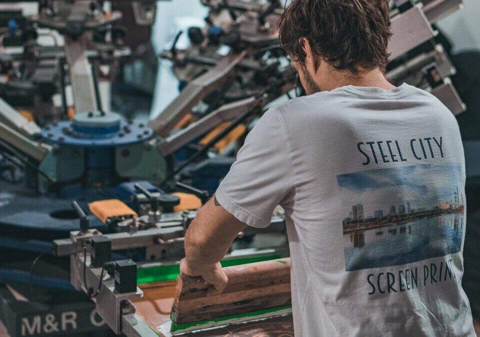 Estampador operando máquina de serigrafia em oficina de camisetas