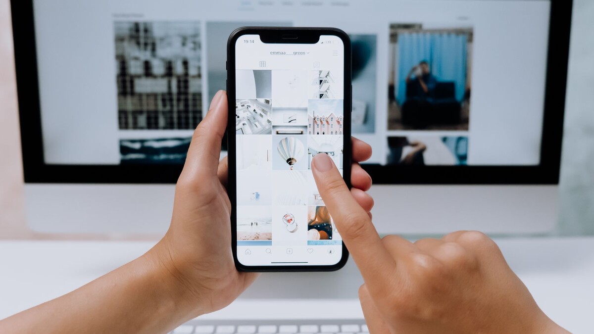 Golpe do iPhone Duo: página falsa ataca o celular só de ser aberta Mãos segurando um iPhone e navegando em uma página diante de um monitor