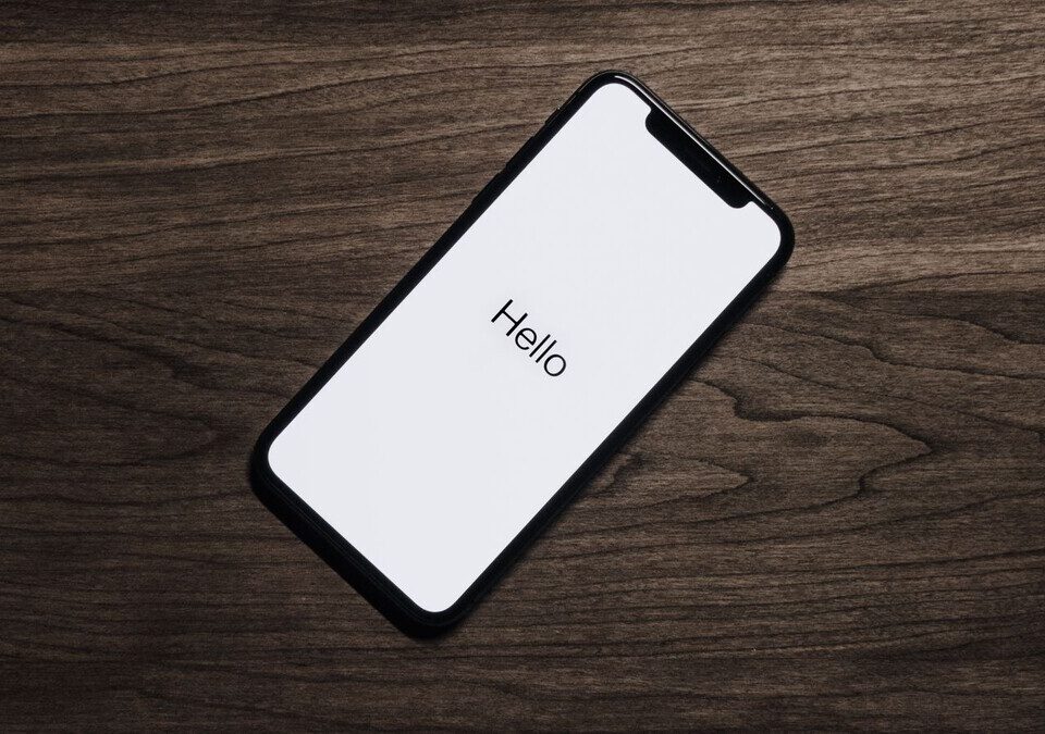 iPhone apoiado sobre mesa de madeira com a tela de boas-vindas acesa