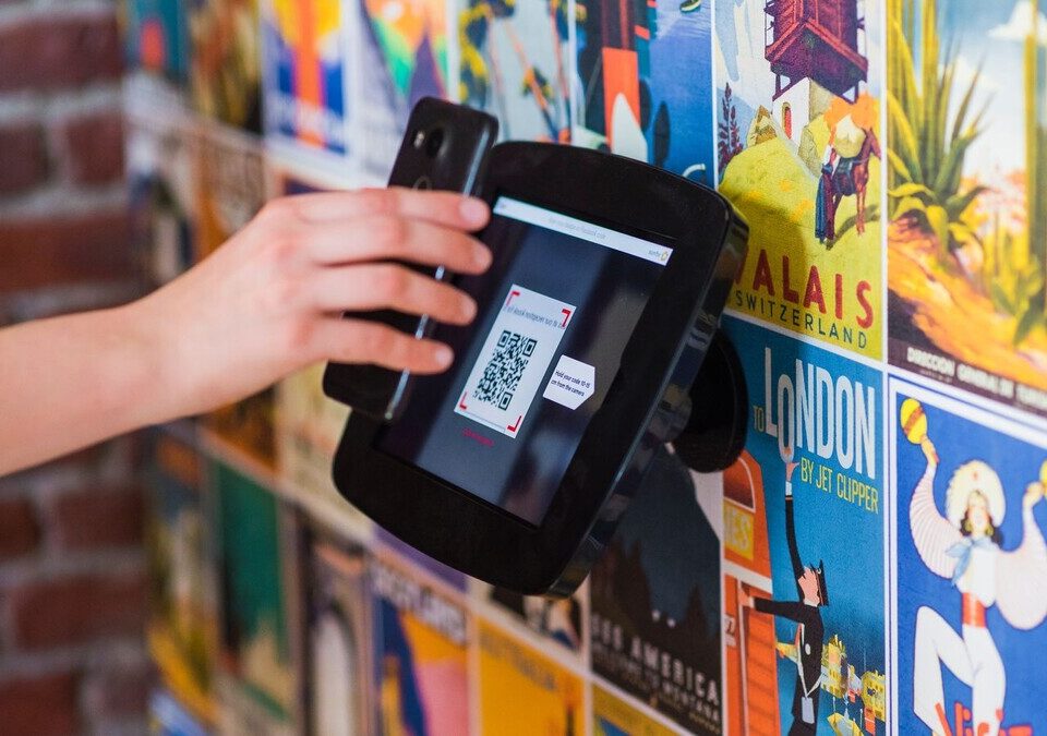 Golpe do QR Code falso: como funciona o quishing e como se proteger Mão segurando celular para escanear um QR Code em um balcão