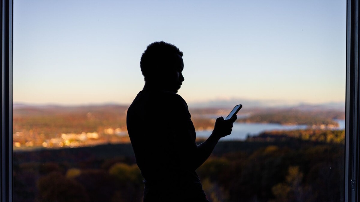 Internet via satélite no celular: Brisanet e Unifique fecham acordo Silhueta de pessoa usando o celular diante de uma janela com paisagem ao entardecer