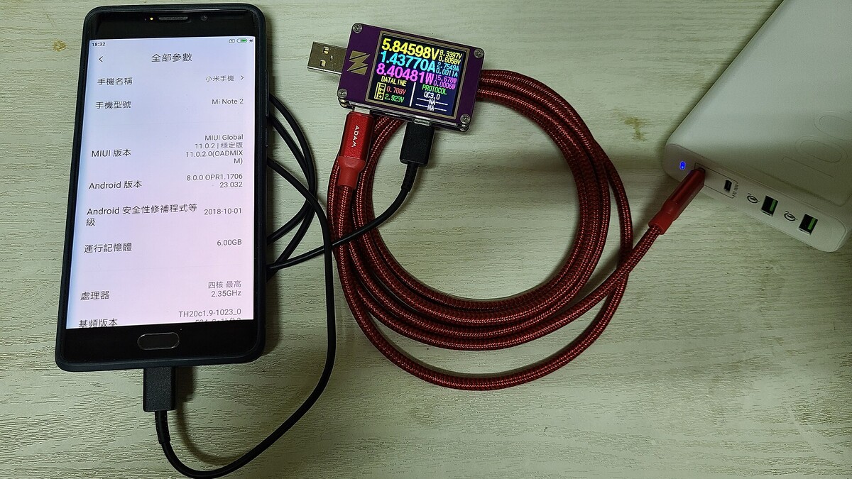 Celular conectado a cabo de carregamento com medidor USB indicando consumo de energia