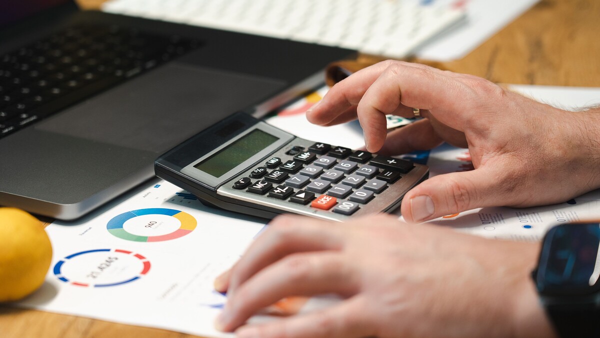 O que são dados próprios e como usá-los no marketing digital? Pessoa usando calculadora ao analisar gráficos e documentos em uma mesa.