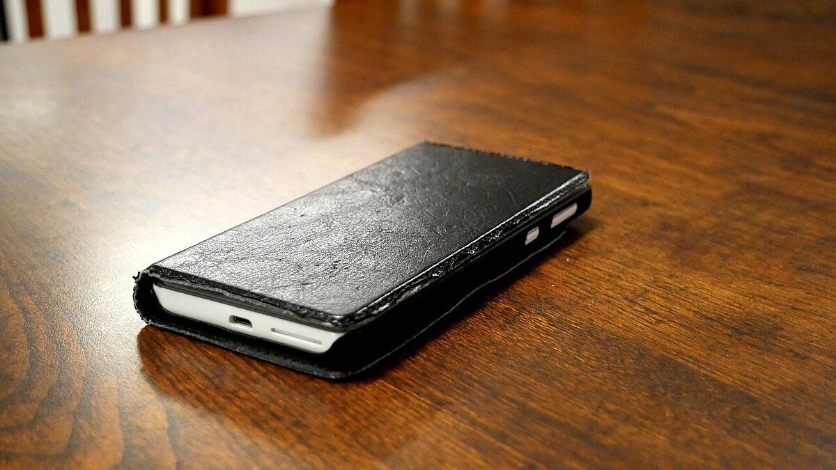 One UI 9 chega ao Galaxy A36 e A56: quando sai no Brasil e o que muda Celular com capa de couro preta sobre uma mesa de madeira