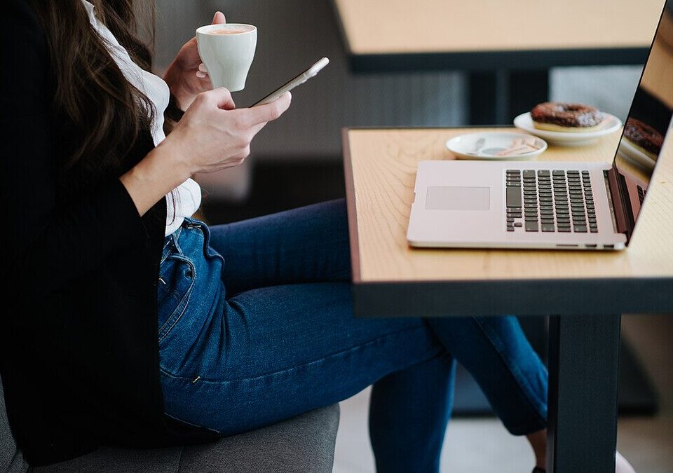 Mulher sentada em um café usando o celular ao lado de um notebook