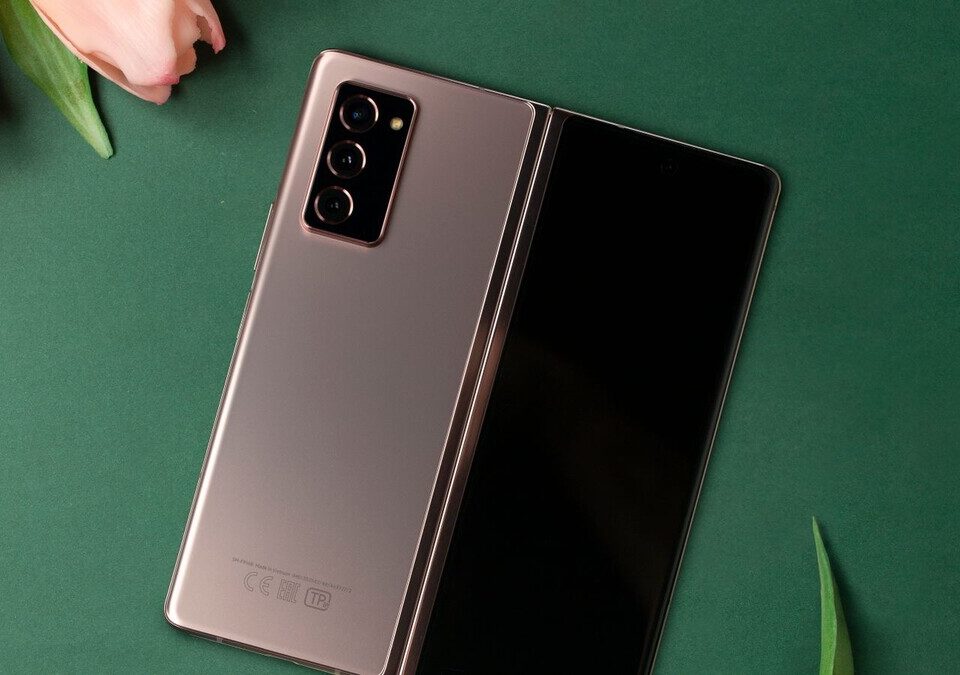 Celular dobrável aberto ao lado de tulipas cor-de-rosa sobre fundo verde